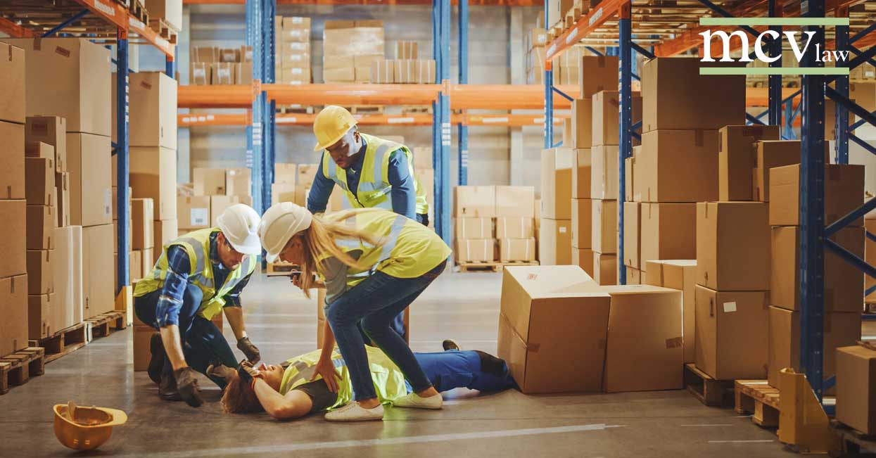 A fallen warehouse worker surrounding by other workers rushing to their aid