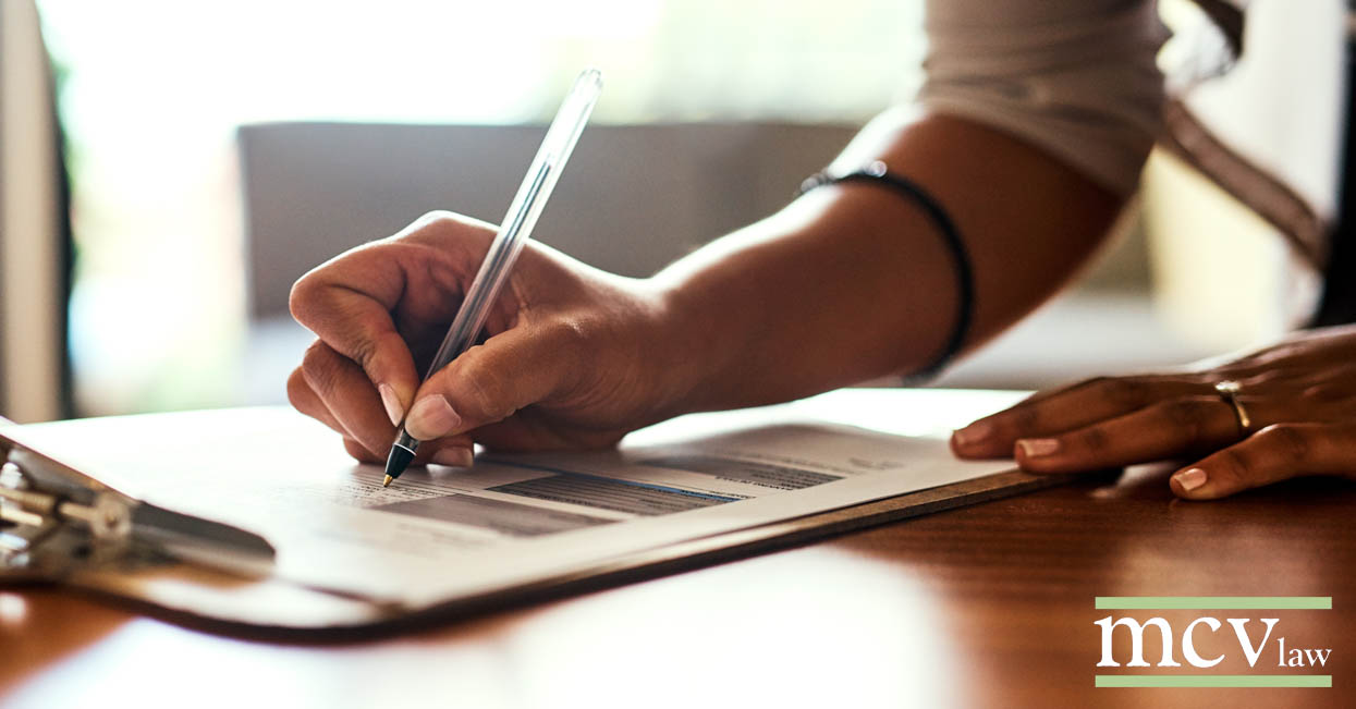 A person's hand signing social security disability application forms on a clipboard