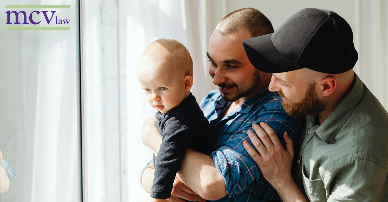 Two men with their baby looking out a window