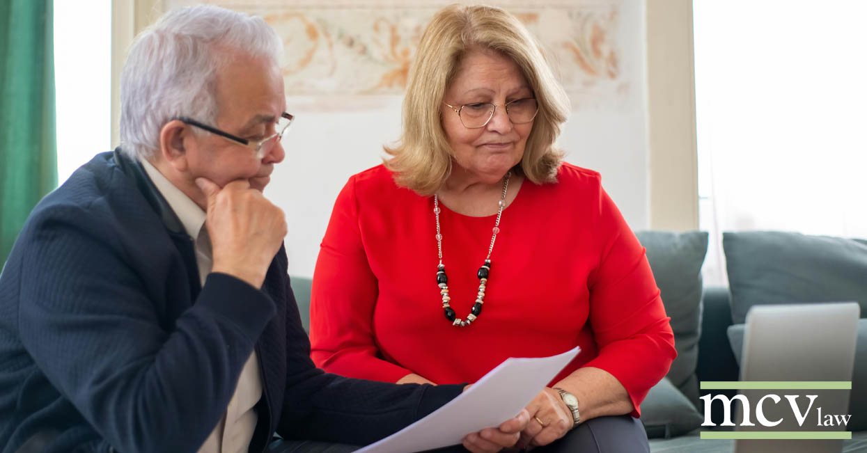 a older couple sternly reviewing paperwork in front of a laptop