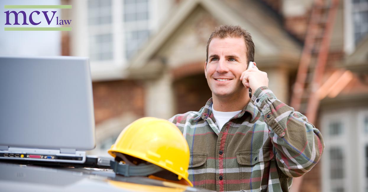 A construction worker on his cell phone with a laptop on site