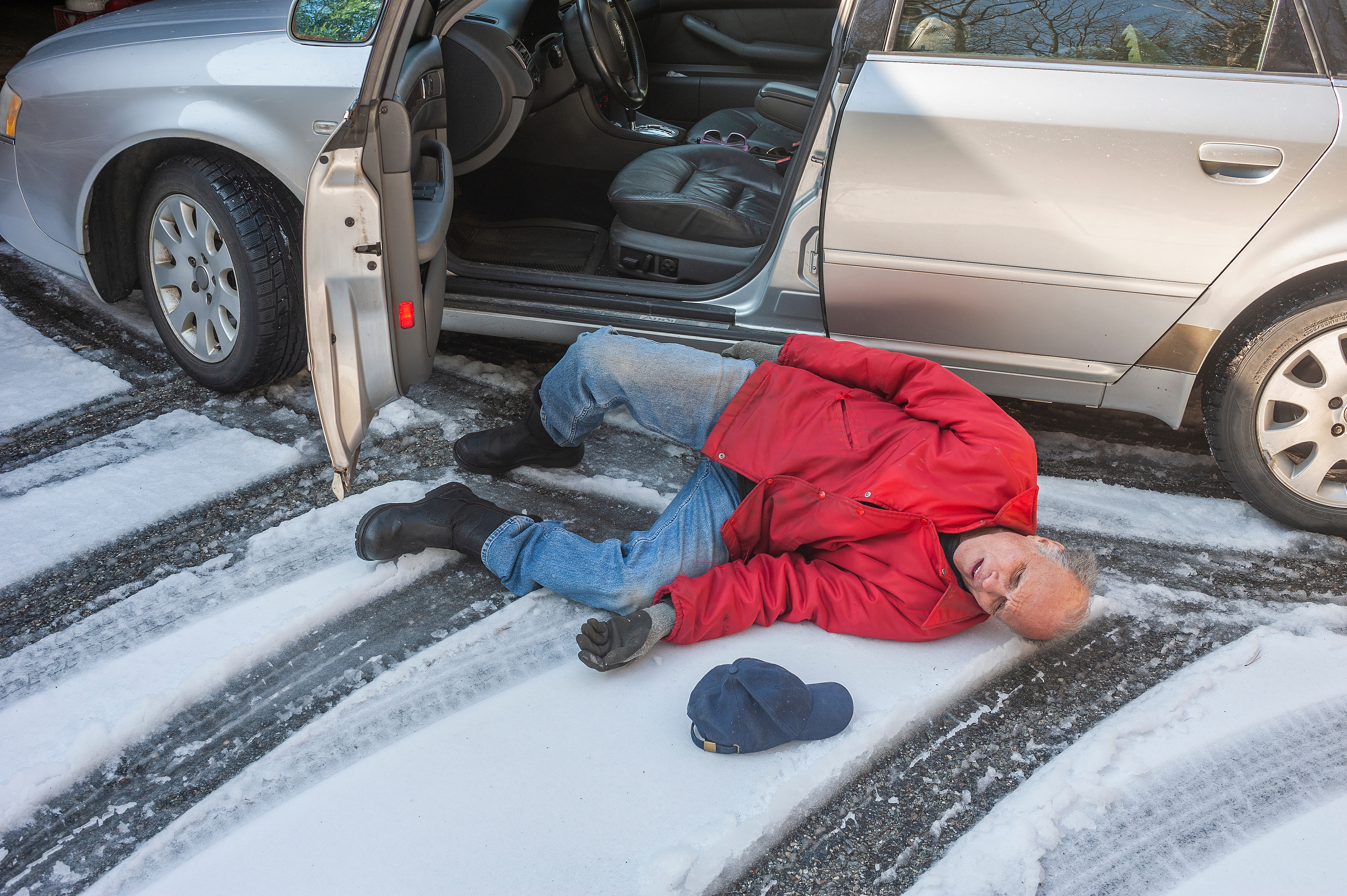 an older man fallen on the snowy ground outside of his car